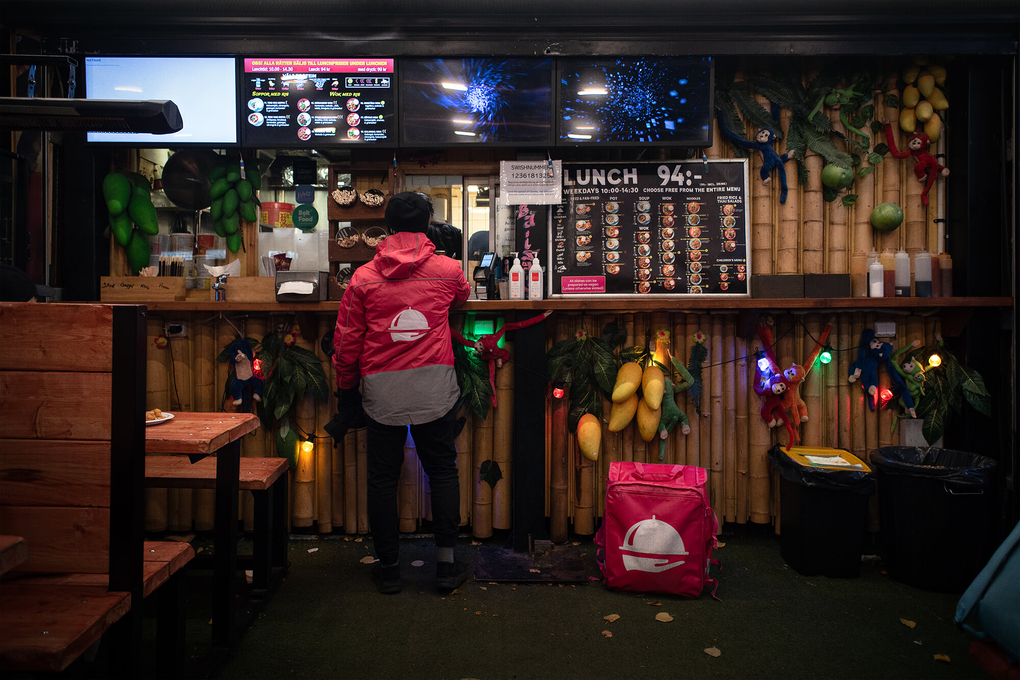 Ett matbud iklädd foodora-jacka väntar på vid en restaurang på en beställning.