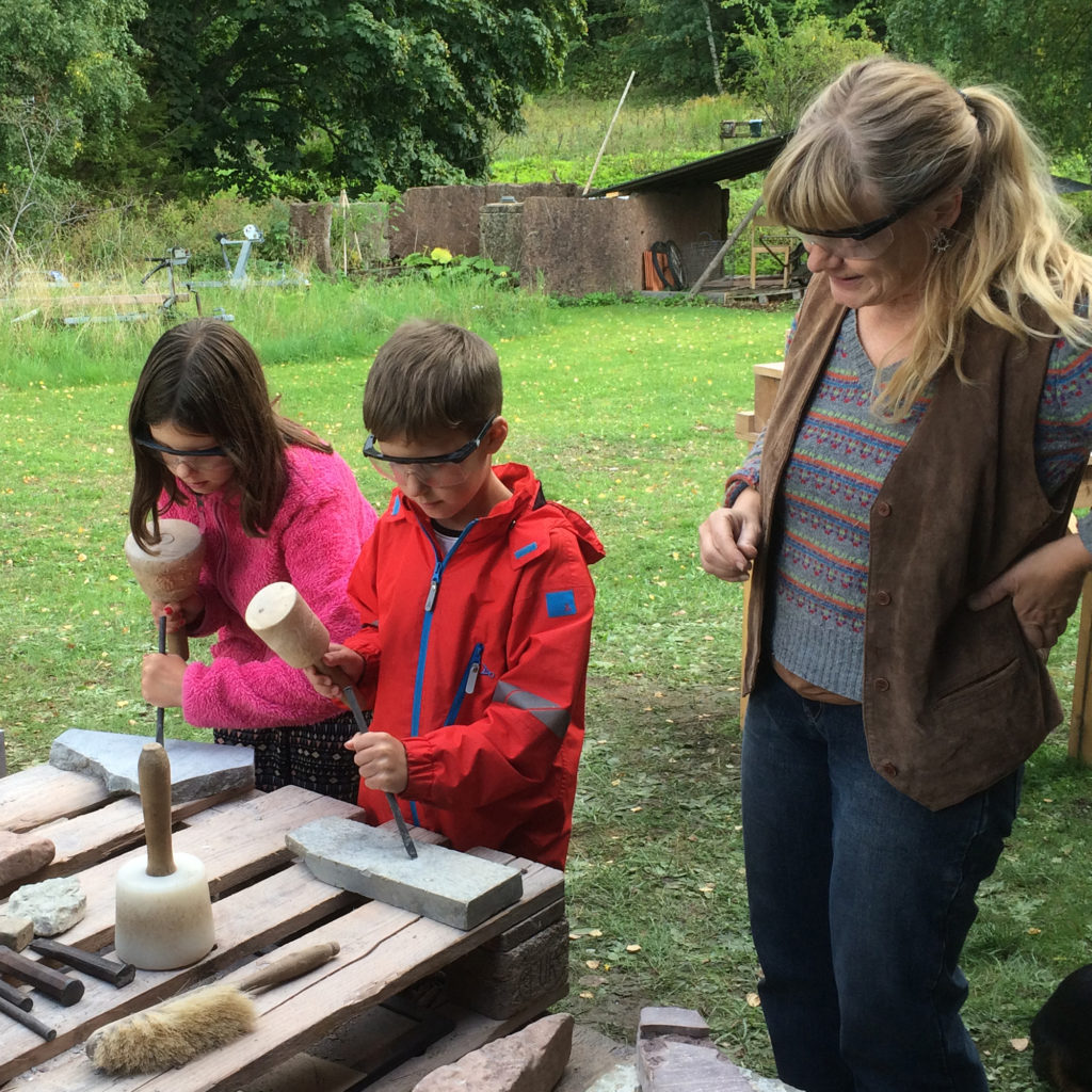 En ledare hjälper två barn lära sig stenhuggeri.