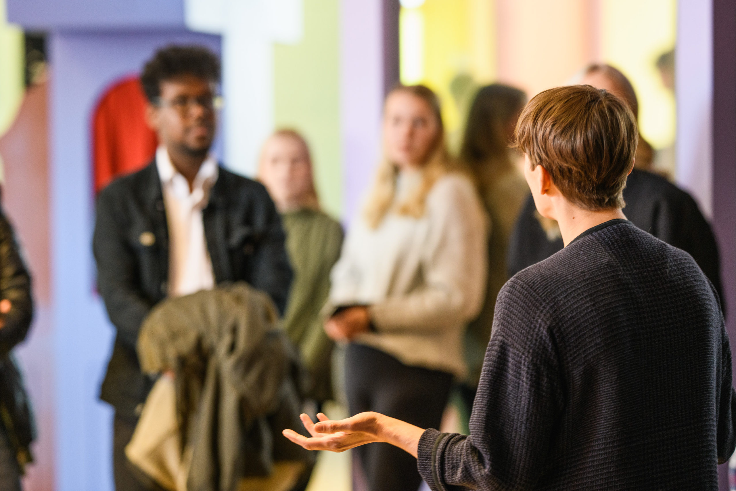 Närbild på en Pedagog presenterar en utställning för flera besökare.