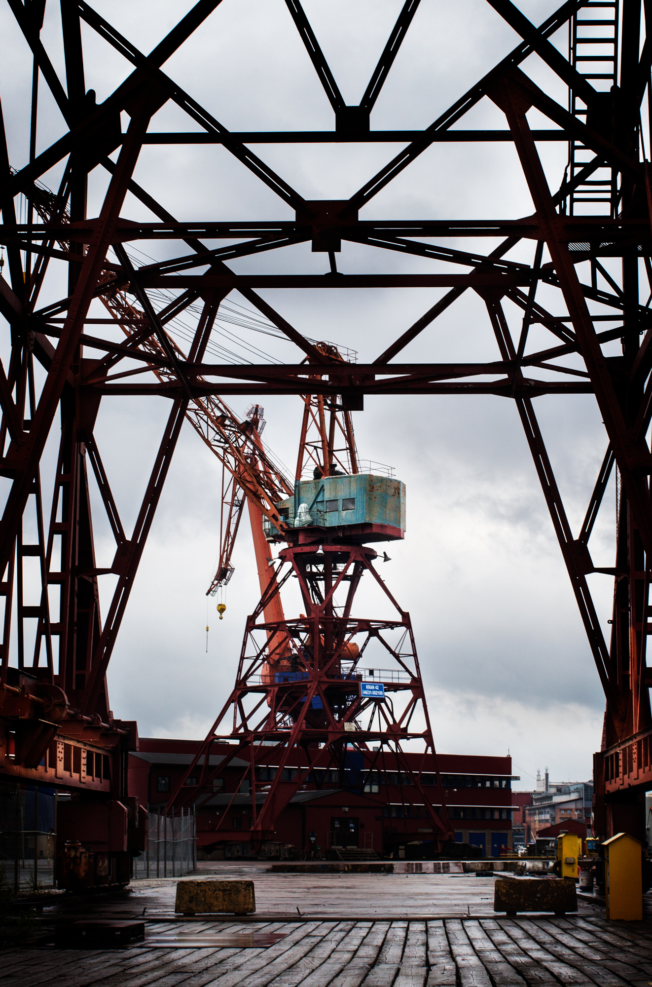 Två roströda kranstrukturer mot en mulen himmel. Industribyggnader i bakgrunden.